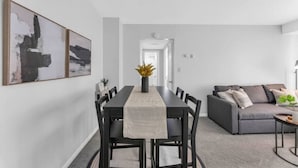 Un salon moderne avec un canapé gris, une table à manger et des chaises, ainsi que des œuvres d’art abstraites accrochées au mur.