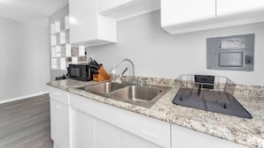 Une cuisine moderne avec des meubles blancs, un plan de travail en granit, un évier en acier inoxydable et un four à micro-ondes.