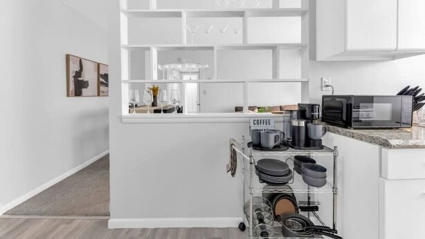 Une cuisine moderne avec des meubles blancs, un coin café et un meuble vitré où sont exposés les ustensiles de cuisine.
