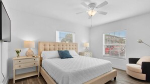 Ein Schlafzimmer mit Bett, Nachttischen, Deckenventilator und Fenstern.