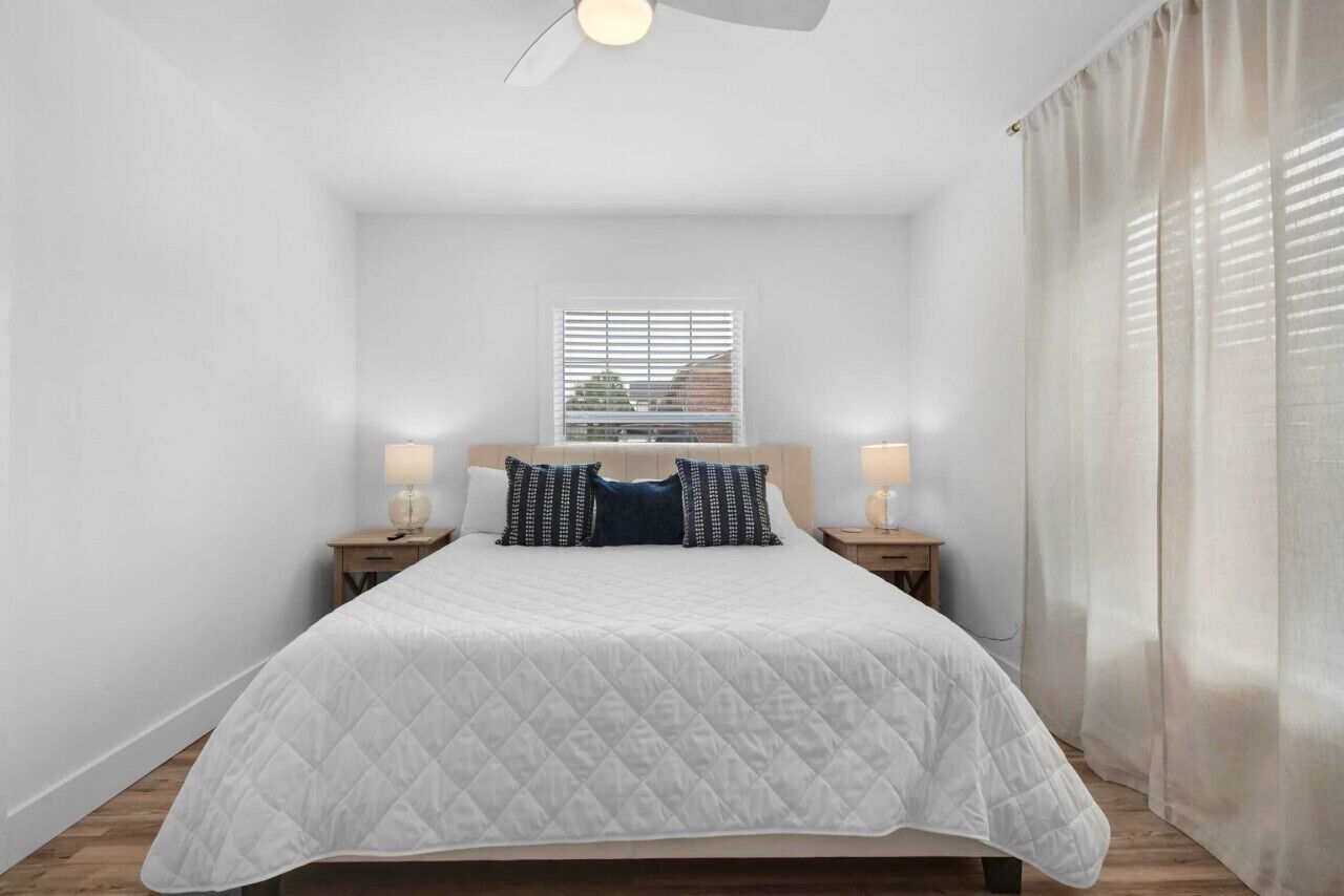 A neatly arranged bedroom with a bed, two bedside tables, a ceiling fan, and a window with blinds.