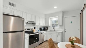 A modern kitchen with white cabinets, stainless steel appliances, and a dining area with wicker chairs. - Heated POOL and SPA-Bluefish #4 - OKA Island 2BR (Fort Walton Beach)