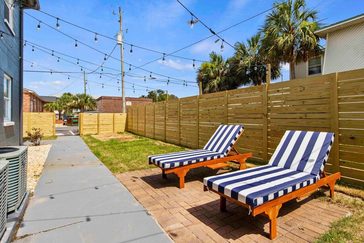 Un patio trasero con dos sillones de madera, una valla de madera y luces colgantes.