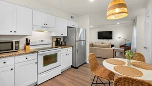 A modern kitchen with white cabinets, stainless steel appliances, and a dining area with a round table and wicker chairs.