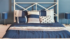 A bed with a geometric headboard, multiple pillows, and bedside lamps. - Modern 3 Bedroom with 85" TV, Air Hockey, BBQ, Ping Pong, Foosball & More (Houston)