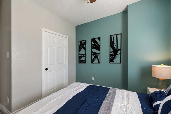 A bedroom with a bed, a door, and three abstract wall art pieces.