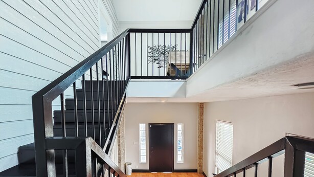 A multi-level interior with a wooden floor, black railings, and a staircase leading to a balcony. - Modern 3 Bedroom with 85" TV, Air Hockey, BBQ, Ping Pong, Foosball & More (Houston)