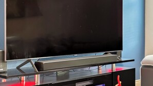 A flat-screen TV on a stand with a decorative red and gold ornament on a round wooden table. - Modern 3 Bedroom with 85" TV, Air Hockey, BBQ, Ping Pong, Foosball & More (Houston)