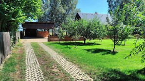 Un sendero pavimentado que conduce a una construcción de madera con techo inclinado, rodeada por una valla de madera y árboles.