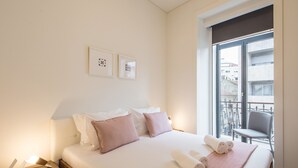 Een hotelkamer met een bed, kussens, een nachtkastje, een raam met uitzicht op gebouwen en een stoel bij het raam.