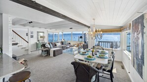 Amplia sala de estar con una mesa de comedor preparada para cuatro personas, un sofá y vista al mar.