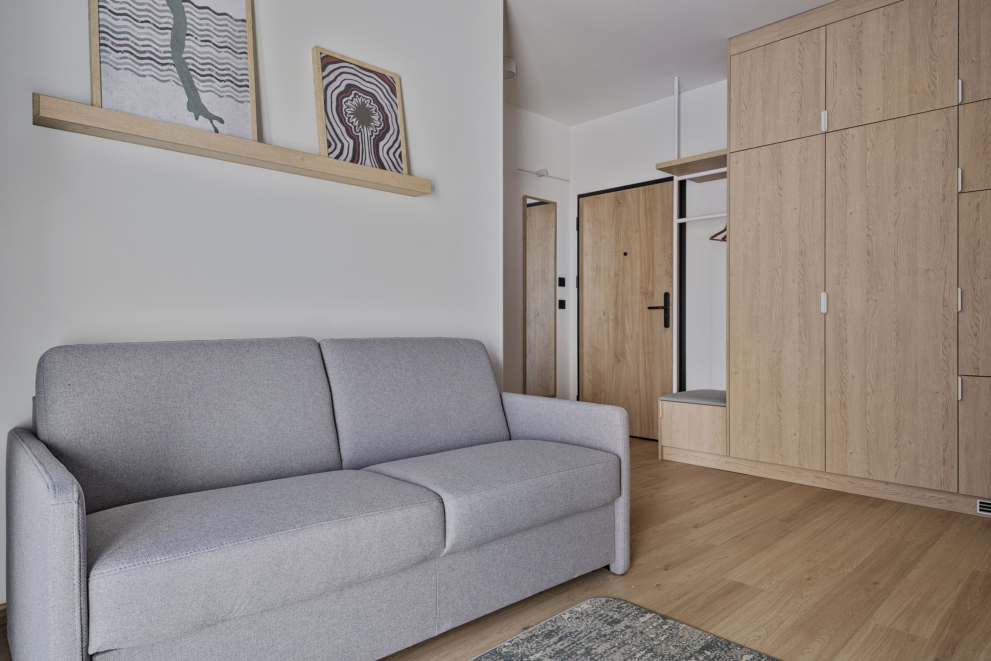 Un salon moderne avec un canapé gris, une armoire en bois et deux œuvres d’art encadrées accrochées au mur.