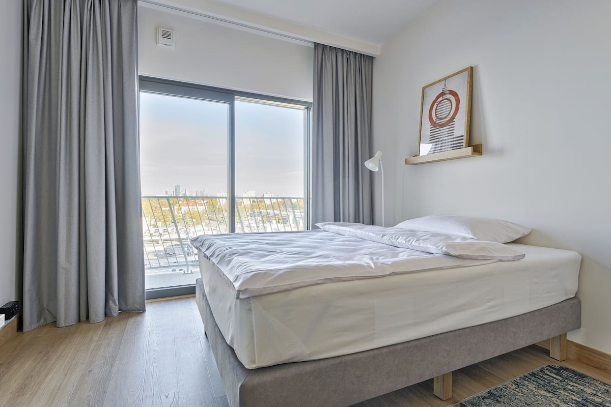 A bedroom with a large window, a bed, and a framed picture on the wall.