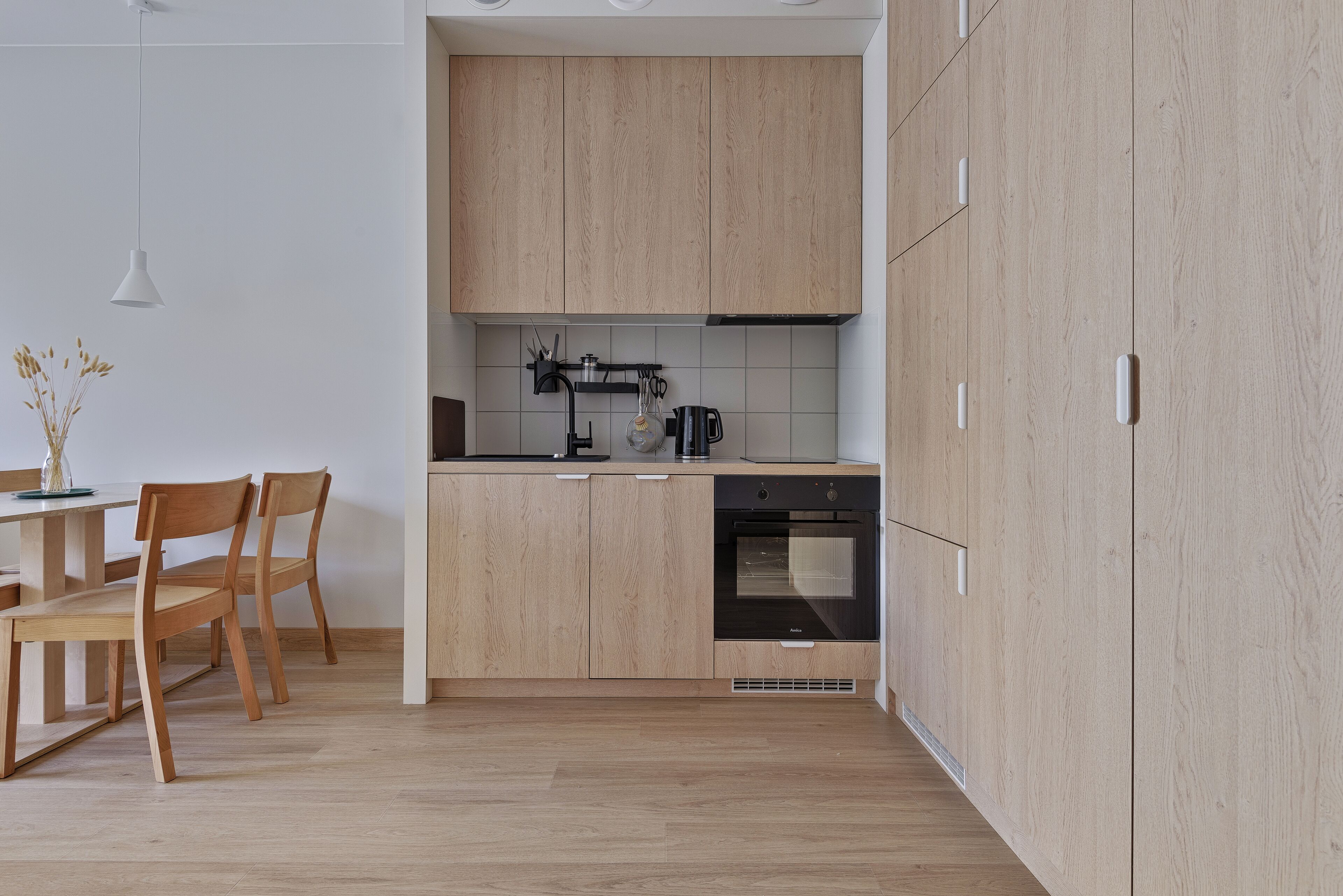 Une cuisine moderne avec des meubles en bois, un four encastré et un coin repas comprenant une table et des chaises.