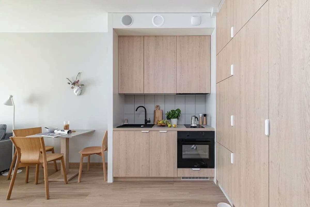A modern kitchen with wooden cabinets, a black oven, and a dining area with a table and chairs.