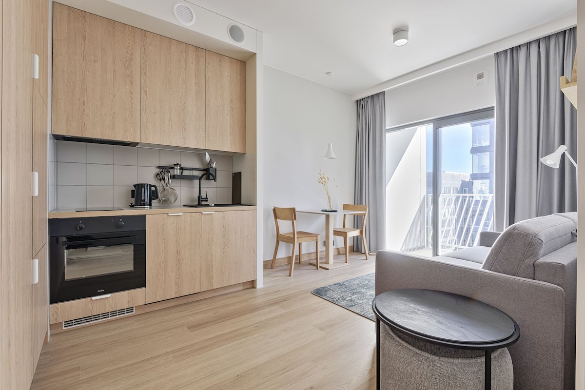 A modern kitchen with wooden cabinets, a built-in oven, and a dining area with a table and chairs.