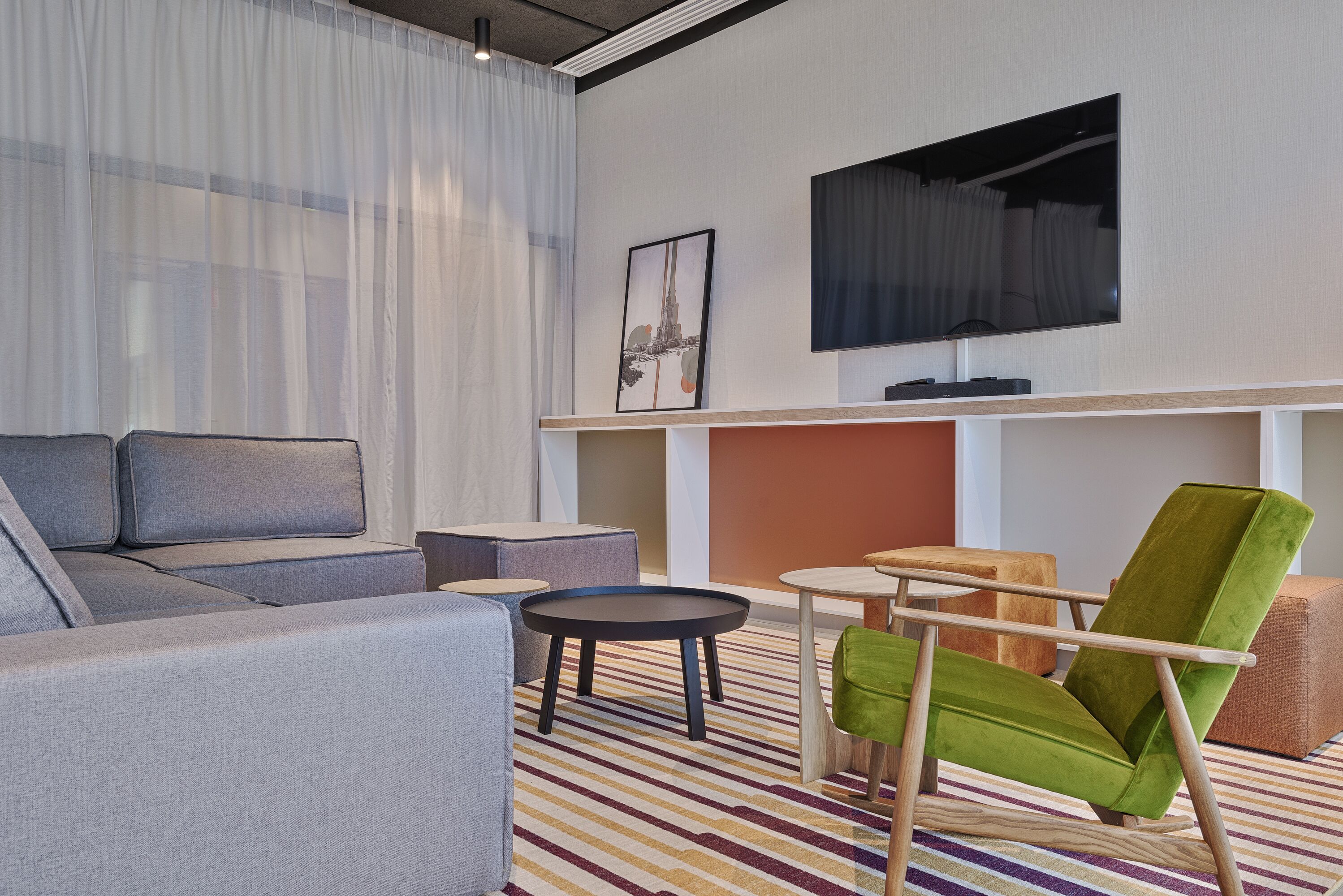 A modern living room with a sofa, armchair, coffee table, and a flat-screen TV mounted on the wall.