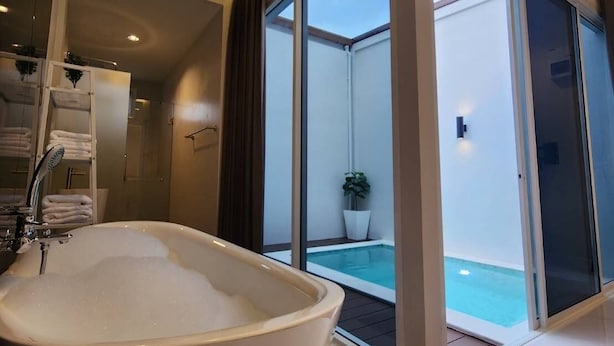 A modern bathroom with a large bathtub, a glass-enclosed shower area, and a view of a pool. - KVILLA (Bangkok)