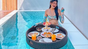 A woman sitting by a poolside table with a variety of food and drinks. - KVILLA (Bangkok)