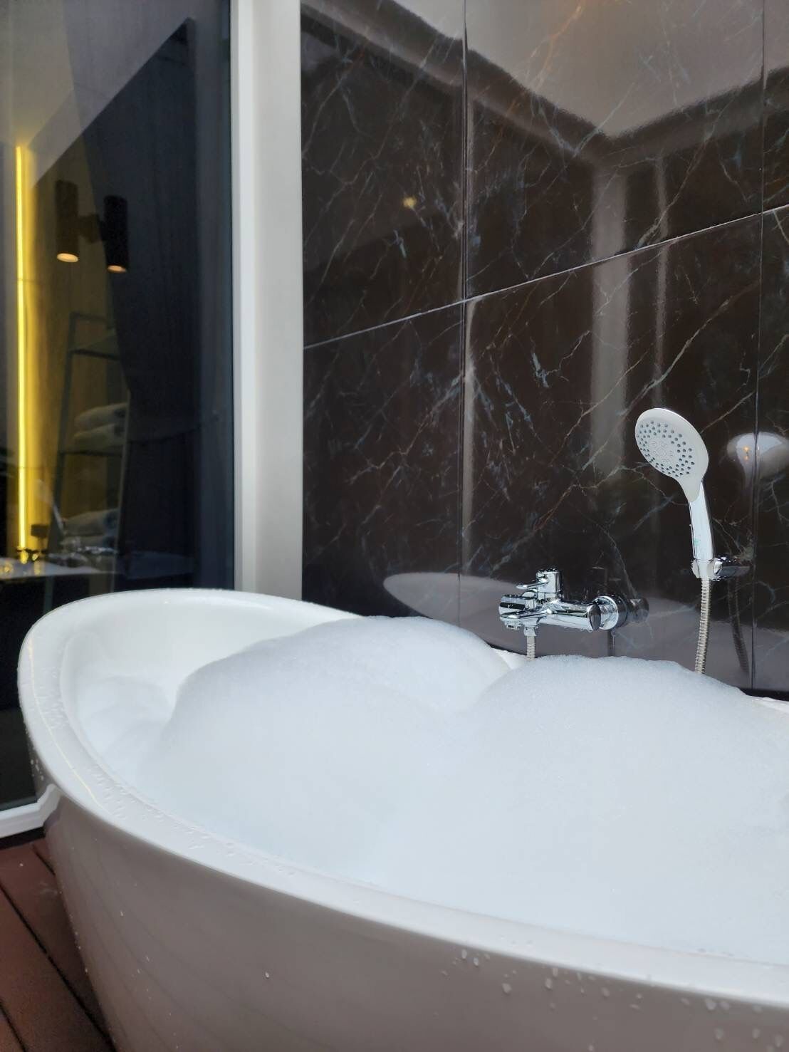 A modern bathroom with a freestanding bathtub, a glass shower enclosure, and a marble-tiled wall.