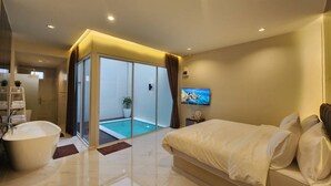 A modern hotel room with a large bed, a bathtub, a glass-enclosed balcony with a pool, and a television on the wall. - KVILLA (Bangkok)