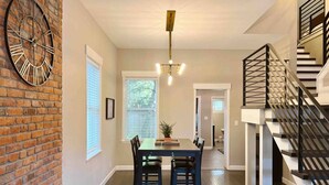 A dining area with a brick wall, a clock, and a staircase. - Enjoy your stay in this cozy, newly renovated condo in the heart of German Village (Columbus)