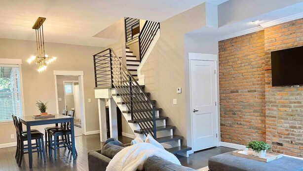 A modern living room with a staircase, a dining area, and a brick wall. - Enjoy your stay in this cozy, newly renovated condo in the heart of German Village (Columbus)