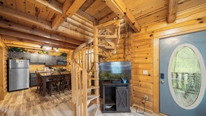 A wooden cabin interior with a kitchen, dining area, and a large window. - Parkway Treasure - 3BR/New Hot Tub/New Firepit/Grill/Sleeps 12 (Gatlinburg)