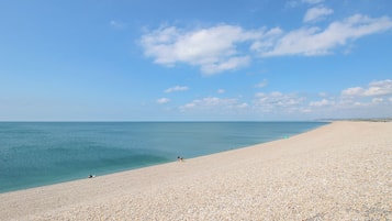 Ein weiter, kieselsandiger Strand mit blauem Himmel und ruhiger See.