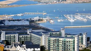 A marina with boats, a coastal town in the background, and modern buildings with balconies.