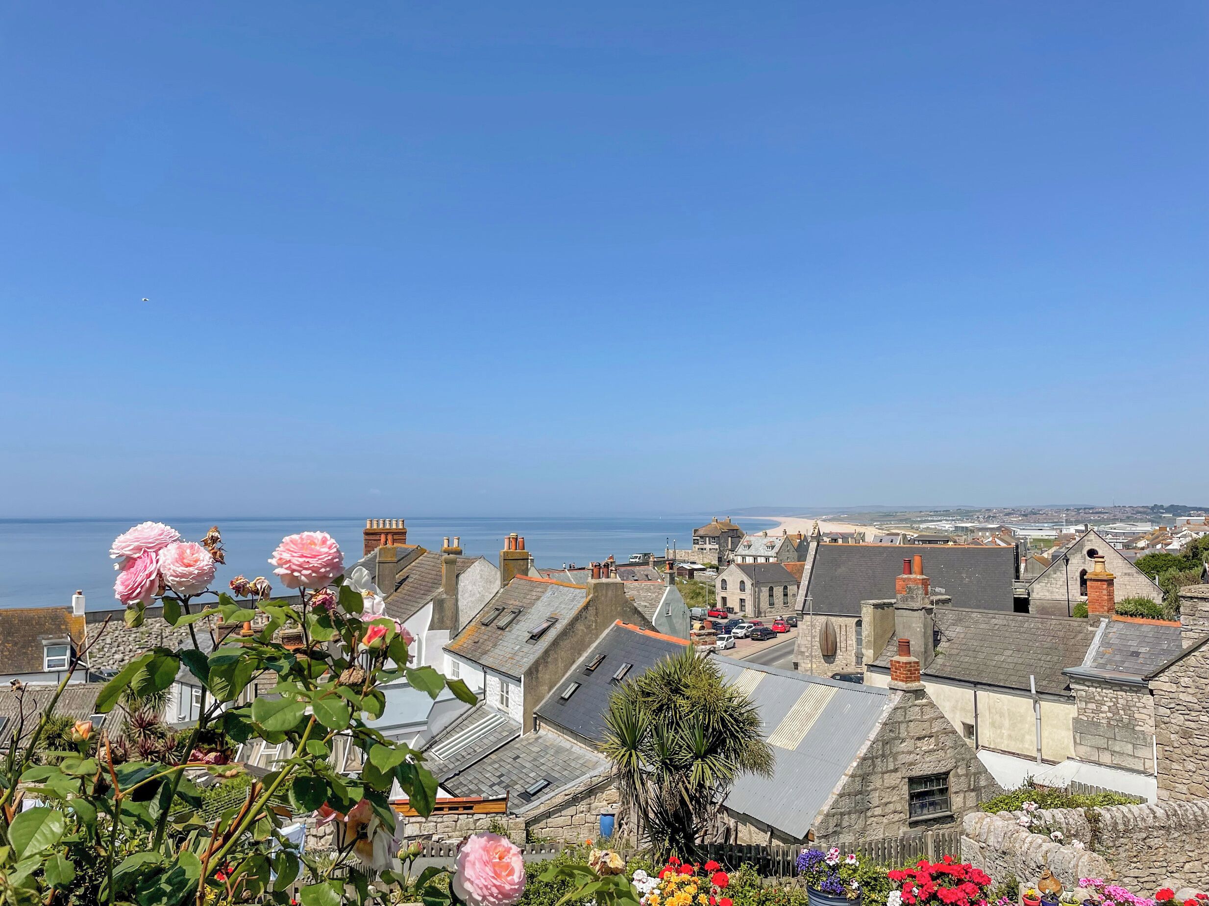 Une ville côtière aux bâtiments en pierre, sous un ciel bleu azur, offrant une vue sur la mer.