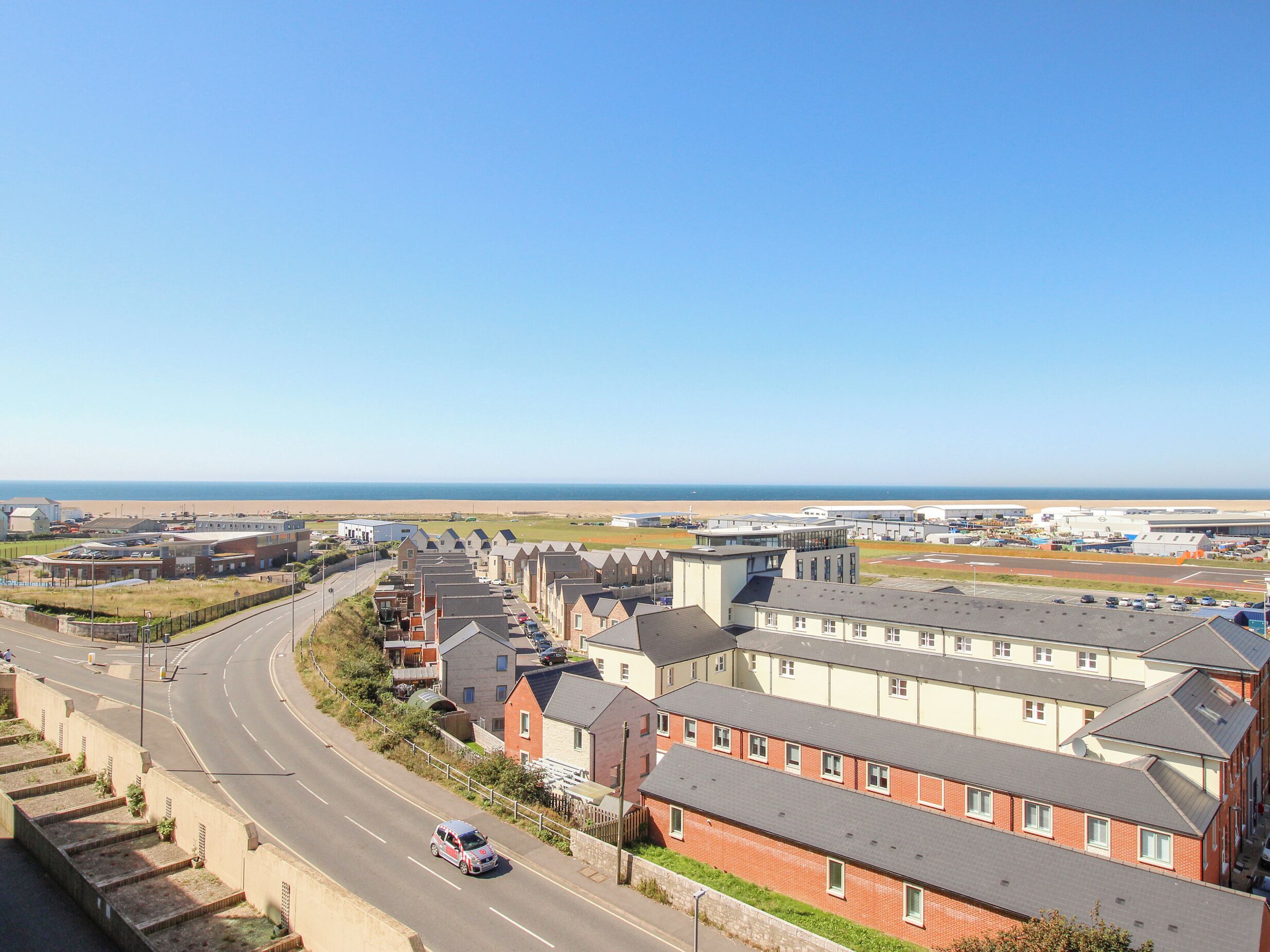A residential area with houses, a road, and a beach in the background.