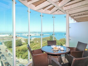 Un balcon avec des fauteuils en osier et une table, donnant sur une marina et un pont.