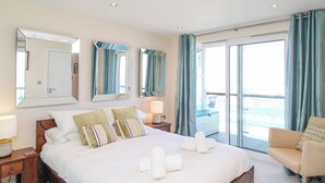 A hotel room with a large bed, two bedside tables with lamps, a chair, and a balcony with curtains.