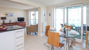 A modern kitchen with a dining area, a TV, and a balcony with a view.