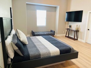 Un dormitorio moderno con una cama, televisión, ventana y una mesita.
