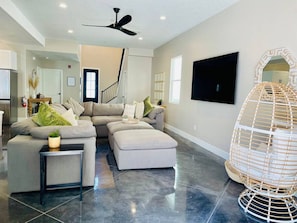 A modern living room with a sectional sofa, a small table, a large flat-screen TV, and a decorative hanging chair.