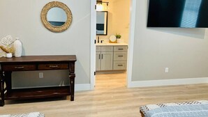 Une pièce avec un bureau en bois, un téléviseur fixé au mur et une porte donnant sur un coin cuisine.