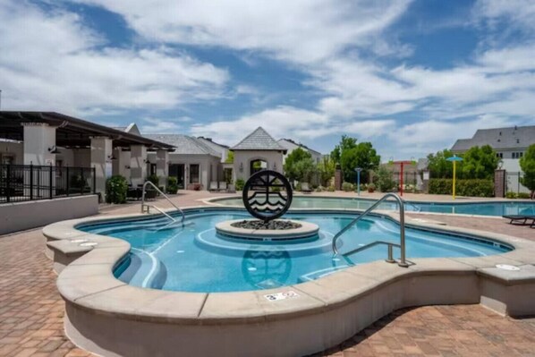 A swimming pool with a decorative sculpture in the center, surrounded by a paved deck and a covered area with columns.