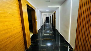 Un couloir d’hôtel avec des portes en bois d’un côté, un sol en marbre noir poli et des murs blancs dotés d’un éclairage encastré.