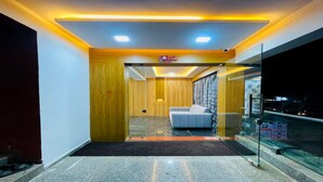 Un hall d’hôtel moderne avec une cloison en verre, un canapé gris et un mur décoratif en bois.