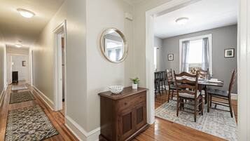 A hallway with wooden flooring, a dining area with a table and chairs, and a mirror on the wall.