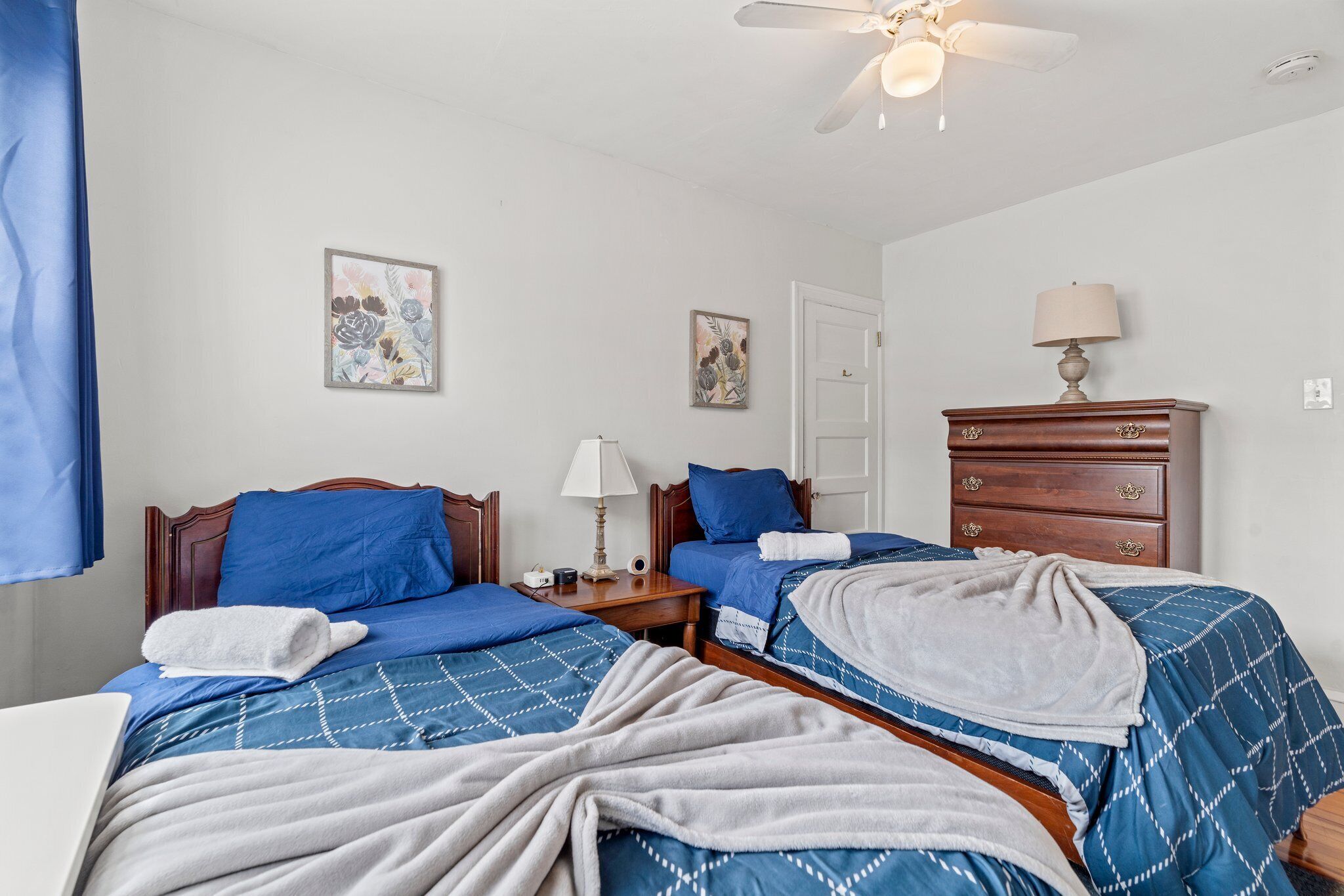 A bedroom with two beds, a dresser, and a ceiling fan.