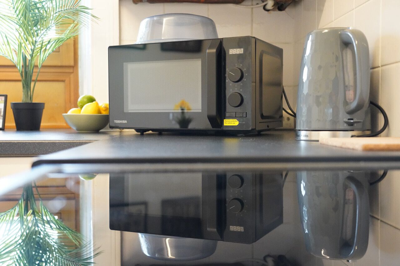 Une cuisine équipée d’un four à micro-ondes, d’un grille-pain et d’un saladier rempli de fruits, posé sur le comptoir.