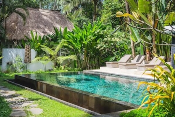 Relax by the serene pool surrounded by lush greenery and tropical plants, with lounge chairs on a raised platform.
