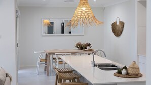 A modern kitchen with a white island, wooden chairs, a hanging light fixture, and a mirror on the wall. - Spoondrift - 5 Mins Walk to Beach (South West Rocks)