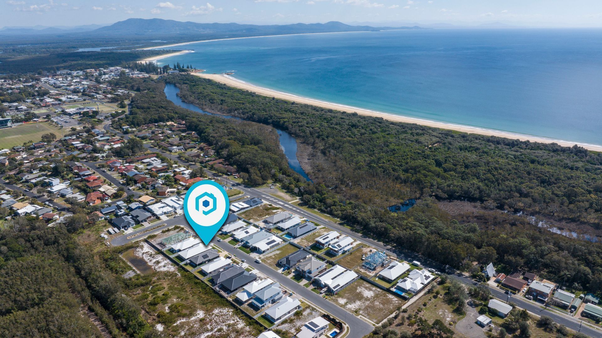 Vue aérienne d’un quartier résidentiel situé sur la côte, avec une plage, une rivière et un ensemble de bâtiments modernes.