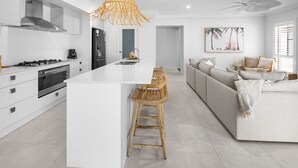 A modern kitchen with white cabinetry, a central island, and wooden bar stools. - Spoondrift - 5 Mins Walk to Beach (South West Rocks)