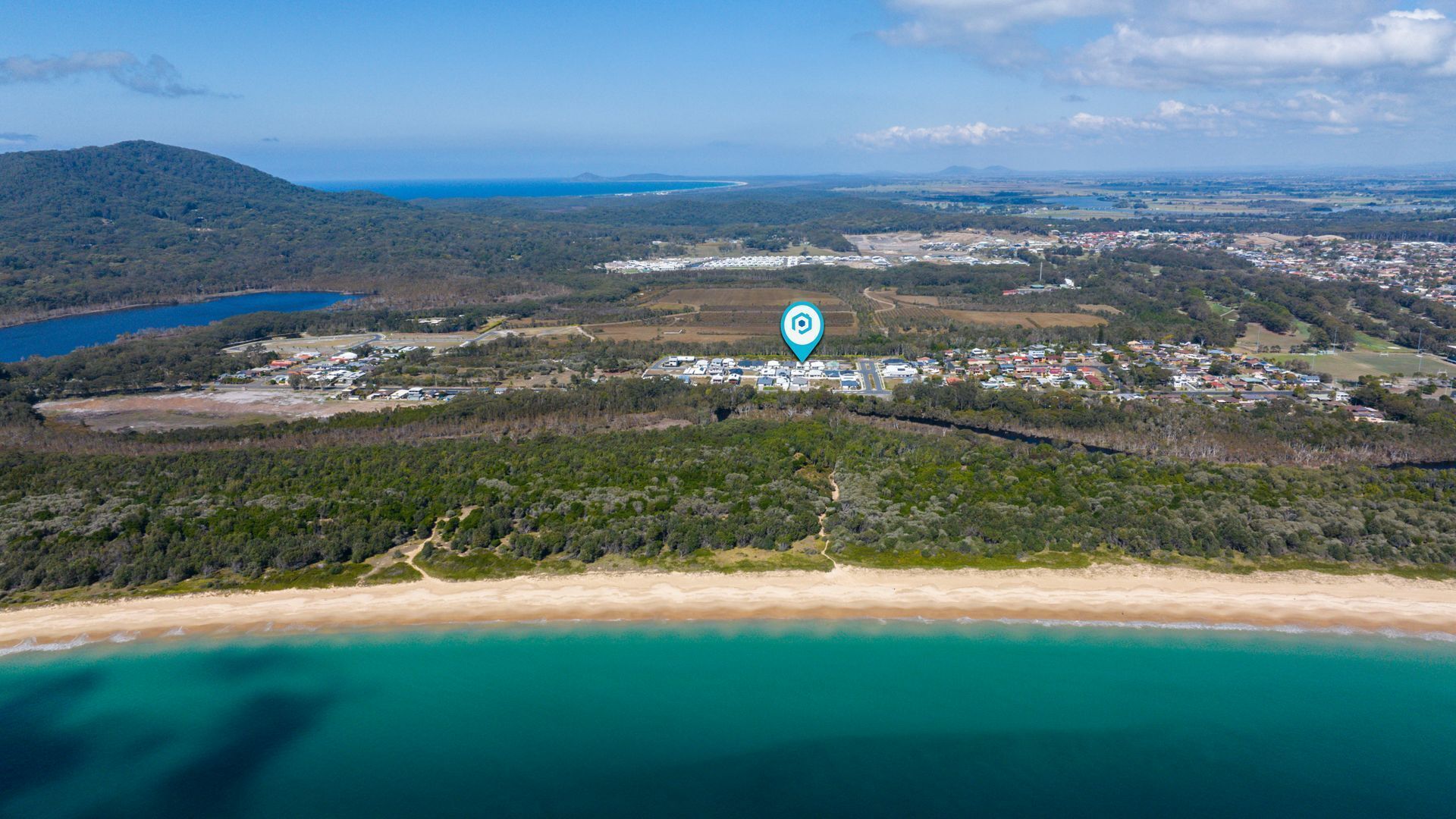 An aerial view of a coastal area with a beach, a small town, and a large industrial complex.