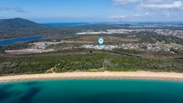An aerial view of a coastal area with a beach, a small town, and a large industrial complex.